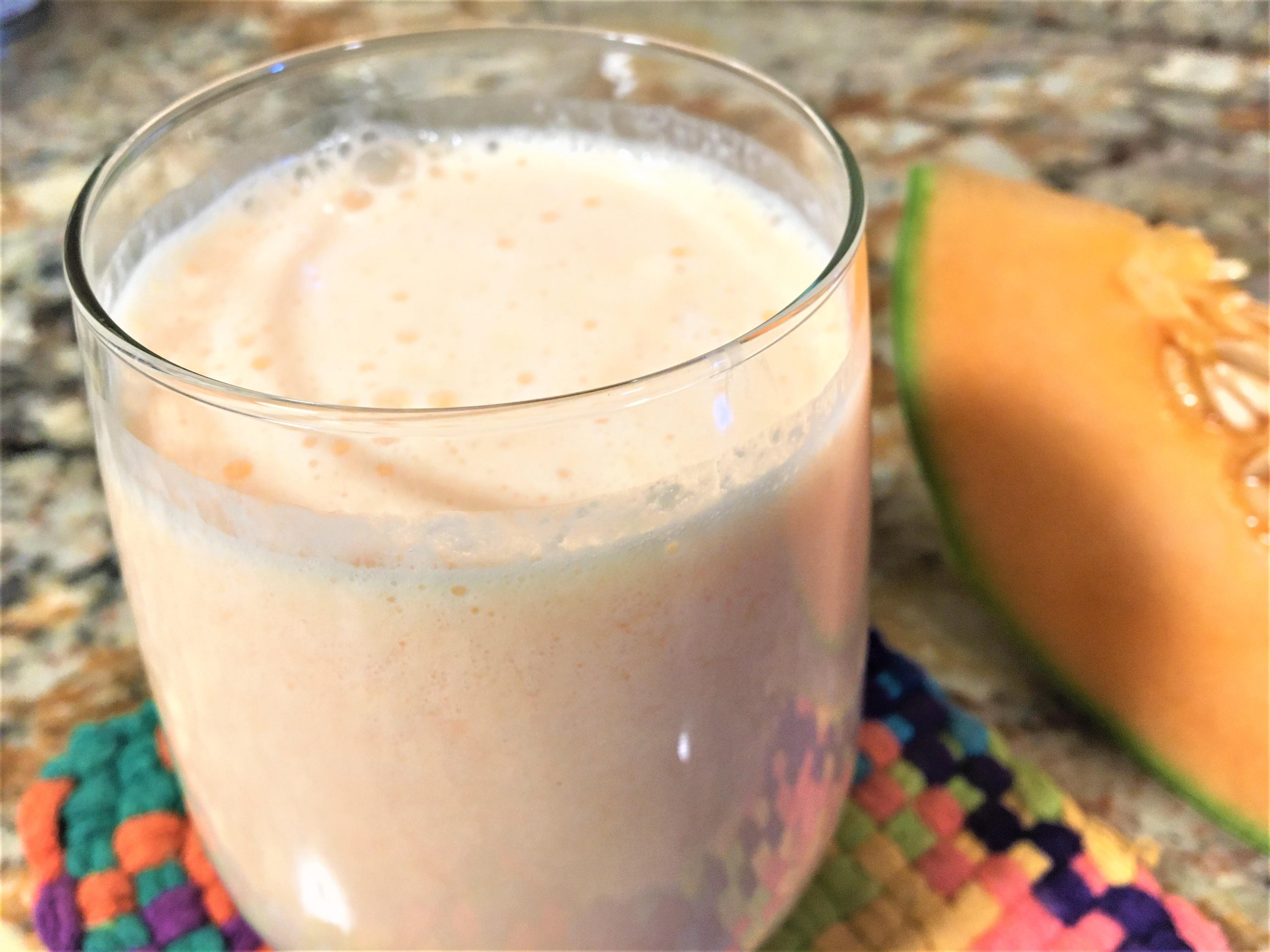 Cantaloupe smoothie with a slice of cantaloupe to the side and colorful potholder at the bottom.