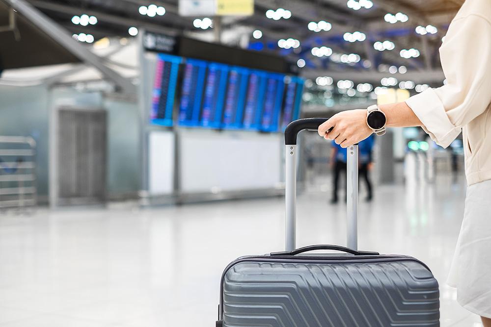 Young woman hand holding luggage handle before checking flight time in airport.