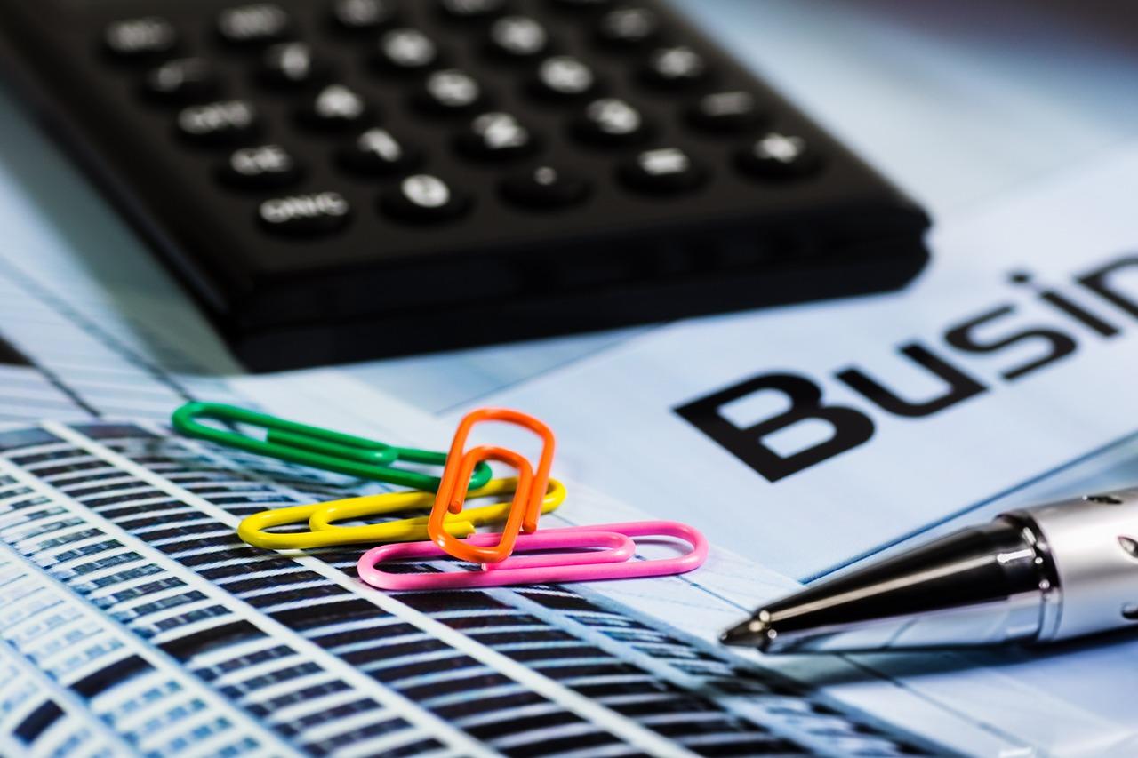 Calculator, paper clips, and pen laying on a spreadsheet