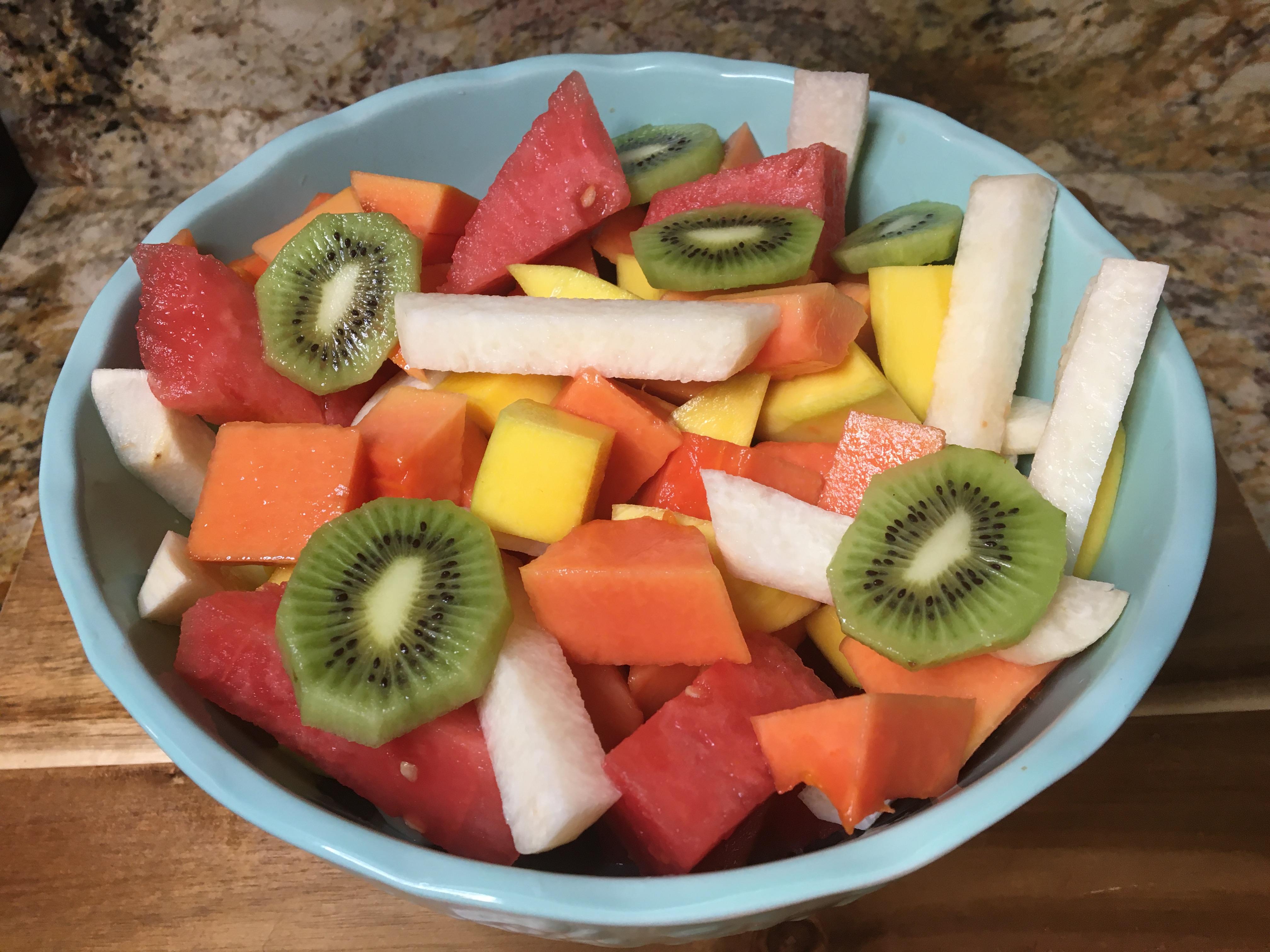 A variety of fruits cut up in a clear bowl.