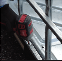 A person using a drill to remove screws from the metal frame.